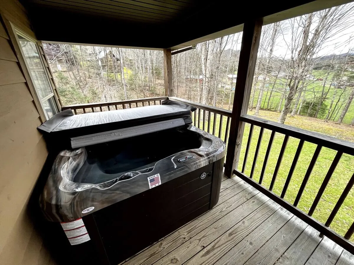 An outdoor hot tub sits beside a wooden railing, overlooking a lush, green landscape. The bubbling tub is perfectly positioned for sunset sessions or stargazing, offering both seclusion and an immersive connection with nature.