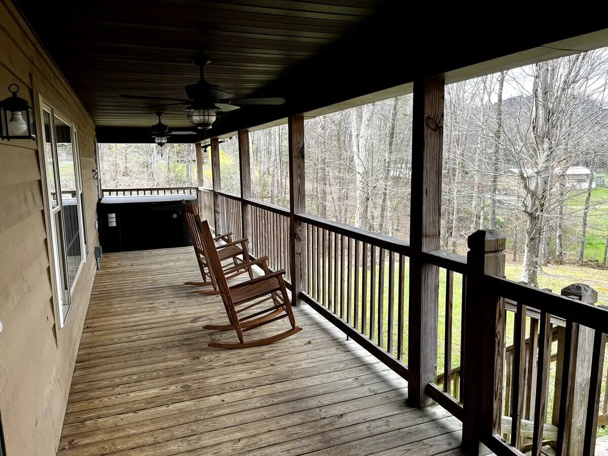 The photo features a cozy deck with classic wooden rocking chairs overlooking a lush canopy of trees. The view from the deck is calm and inviting, suggesting a perfect spot for relaxing with a hot drink while observing nature.