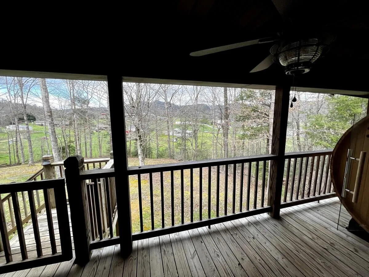 An inviting outdoor deck bordered by a wooden railing, offering sweeping views of trees and distant hills—an idyllic setting for dining or sipping drinks outdoors.