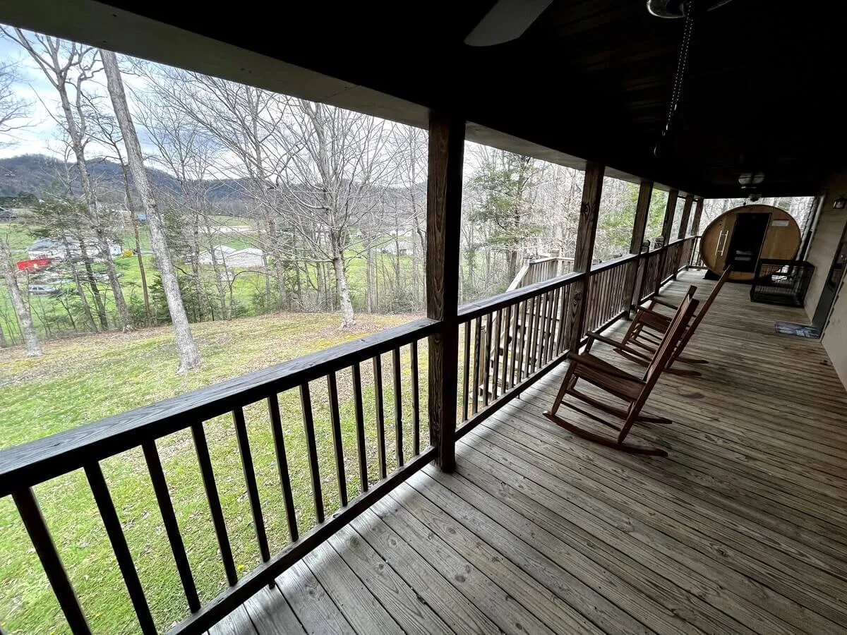 A classic wooden porch with rocking chairs overlooks a sweeping landscape, suggesting peaceful moments spent outdoors. The view hints at mountain vistas and opportunities for guests and pets to unwind together after a day of exploration.