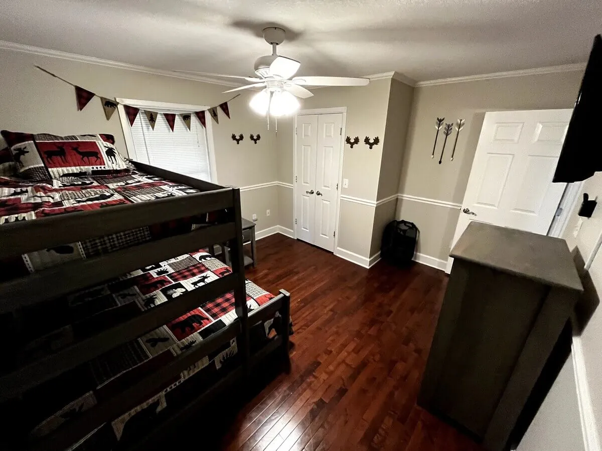 A warm, inviting room with bunk beds adorned in patterned bedding and moose-themed decor. A ceiling fan and soft lighting provide a snug, welcoming environment, ideal for late-night chats or cozy reading sessions.
